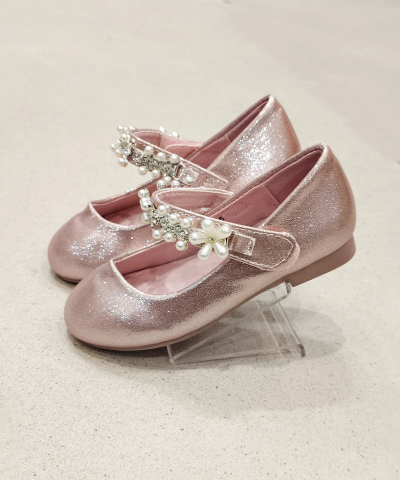 Pair of pink glittery shoes with embellishments on a light background