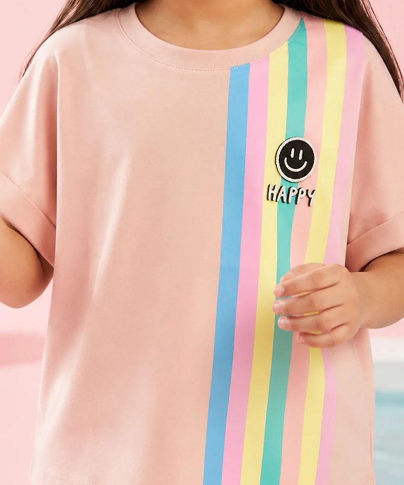 A child wearing a light pink short-sleeve t-shirt with vertical pastel stripes in blue, pink, yellow, and mint green on the right side. A black circular smiley face graphic with the word 'HAPPY' is printed on the chest.