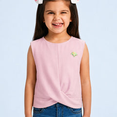 A young girl with a white bunny headband smiles while wearing a sleeveless light pink top with a twisted front detail and a small green and yellow star pin, paired with blue jeans against a light blue background.