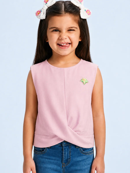 A young girl with a white bunny headband smiles while wearing a sleeveless light pink top with a twisted front detail and a small green and yellow star pin, paired with blue jeans against a light blue background.