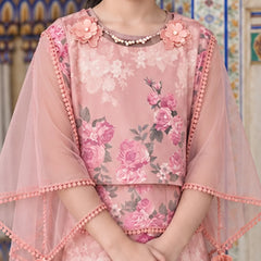 A pink floral embroidered tunic with sheer flutter sleeves, decorated with 3D flowers at the neckline and pom-pom trim, shown on a model in front of a patterned tile wall.