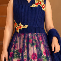 A sleeveless navy blue ethnic dress with a pleated bodice, floral printed tulle skirt, and gold and red embroidered floral details on the chest and waist. The dress is shown on a model against a warm brown background.