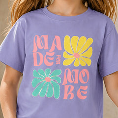 A child wearing a lavender purple t-shirt with a retro-style graphic that reads 'MADE FOR MOBE' in pink and yellow text, accented by two large yellow and green flowers on the front.