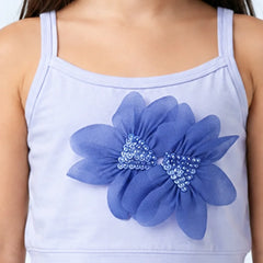 A close-up of a child wearing a light lavender camisole top with a large blue flower applique on the front, featuring blue and silver rhinestone centers.