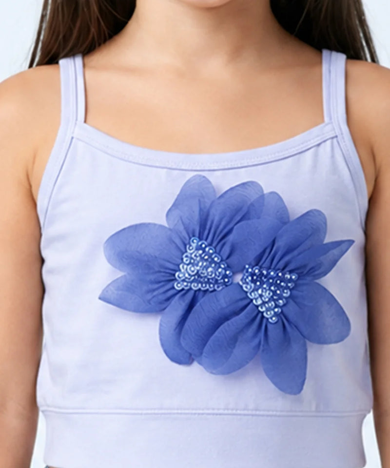 A close-up of a child wearing a light lavender camisole top with a large blue flower applique on the front, featuring blue and silver rhinestone centers.