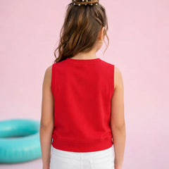 A child viewed from behind wearing a bright red sleeveless crop top and white pants, standing against a solid pink background with a turquoise ring floating in the distance.