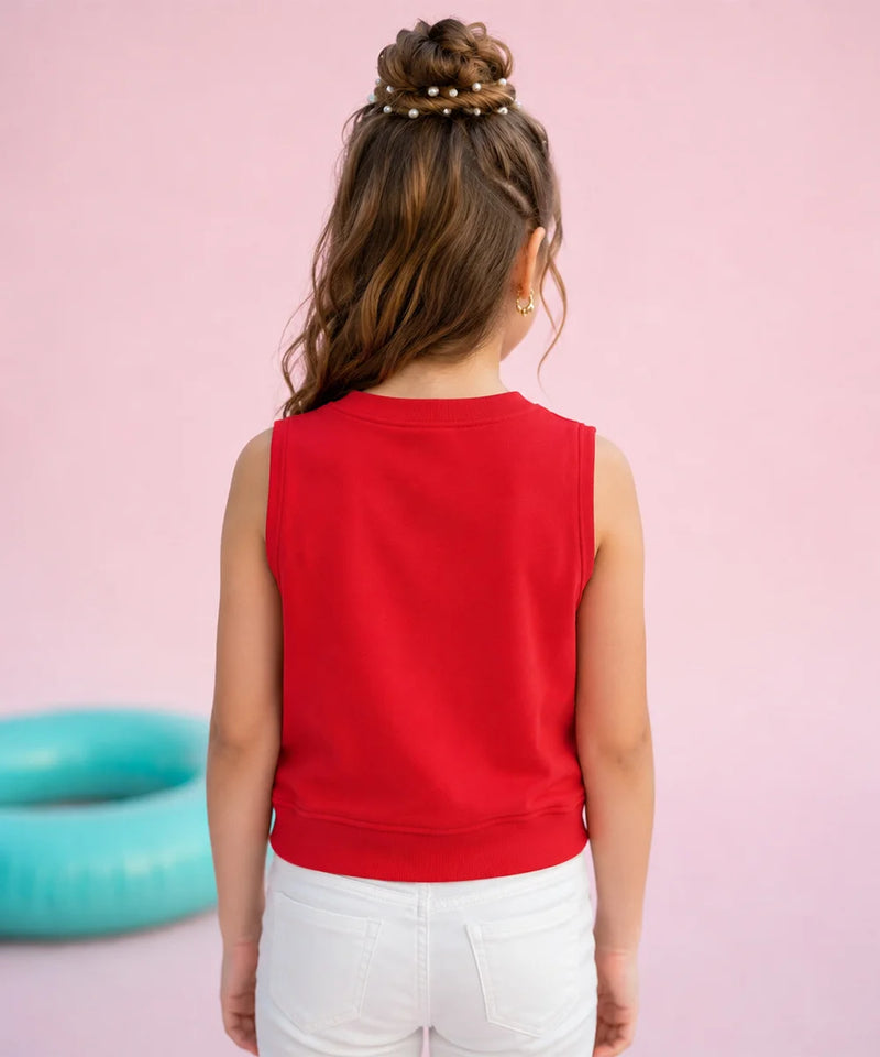 A child viewed from behind wearing a bright red sleeveless crop top and white pants, standing against a solid pink background with a turquoise ring floating in the distance.