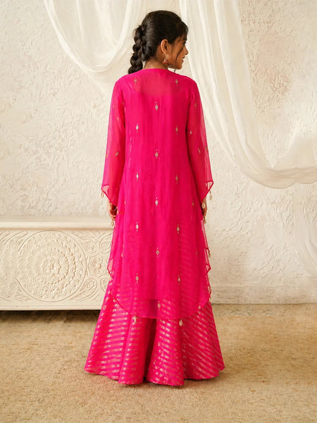 Person wearing a bright pink traditional outfit with a white textured wall in the background