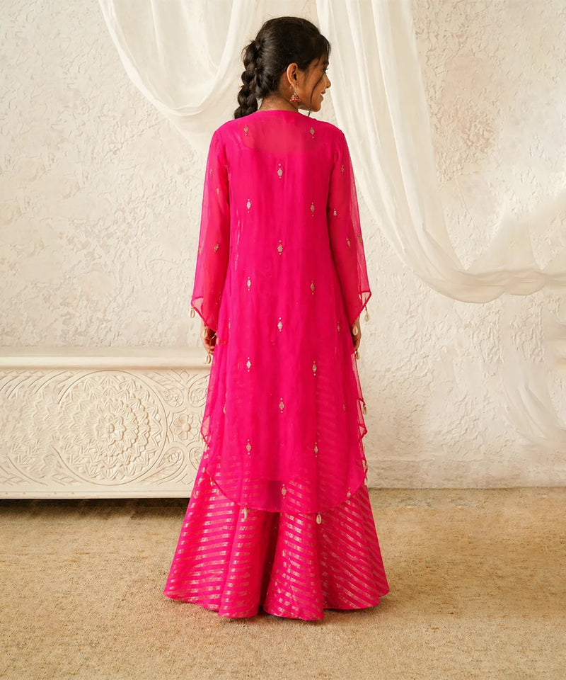 Person wearing a bright pink traditional outfit with a white textured wall in the background