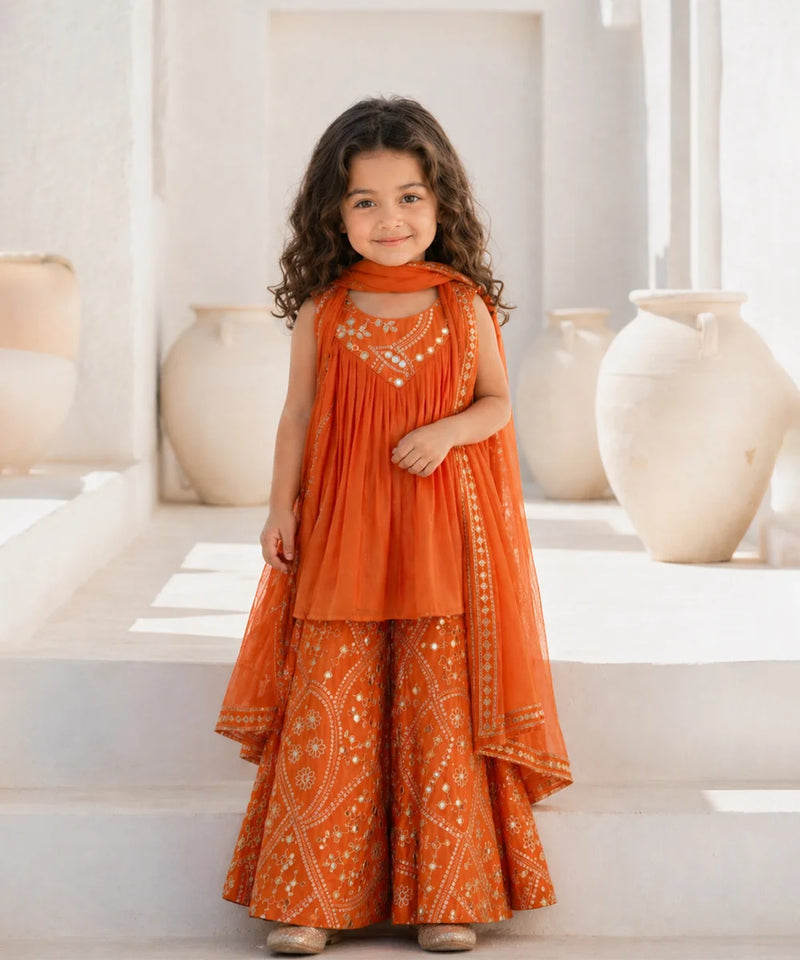 Young girl in an orange traditional outfit standing in a bright room with decorative vases.