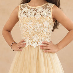 A sleeveless young girl's dress with a cream floral lace bodice and a flowing champagne tulle skirt, shown on a model against a warm beige background.