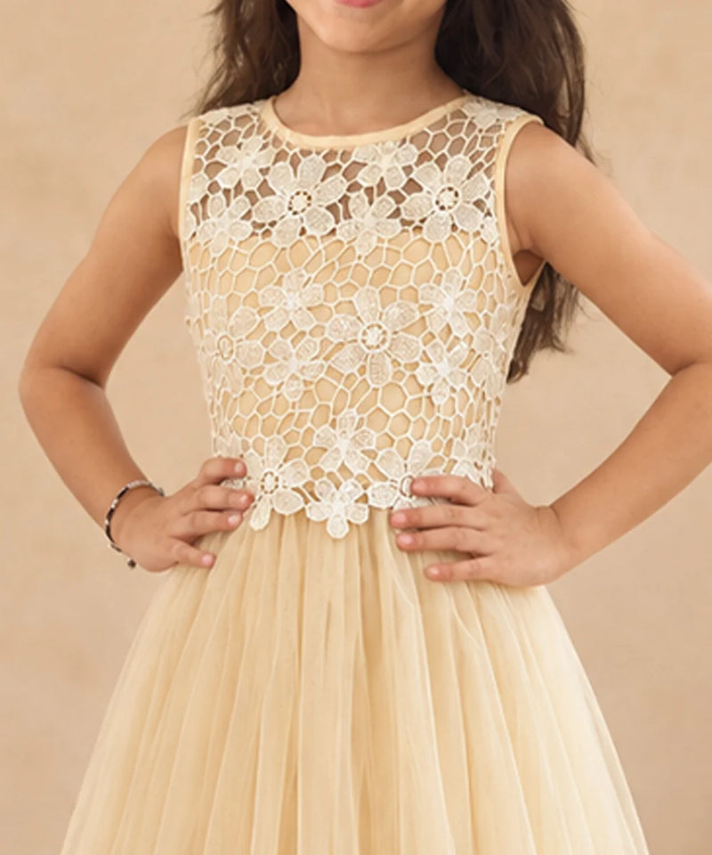 A sleeveless young girl's dress with a cream floral lace bodice and a flowing champagne tulle skirt, shown on a model against a warm beige background.