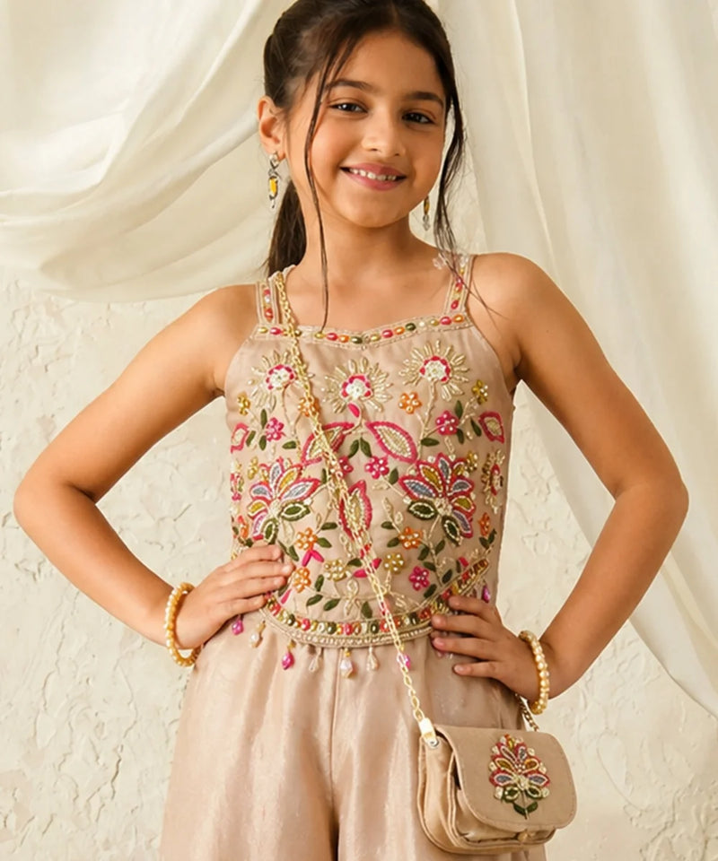 Young girl in a pink traditional outfit with a matching bag against a beige wall.