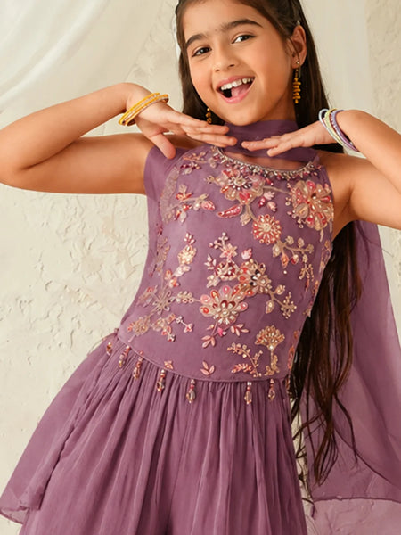 Young girl wearing a purple embroidered dress against a plain background