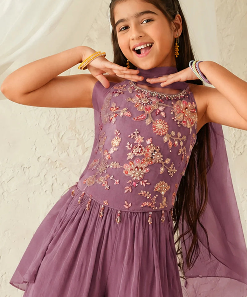 Young girl wearing a purple embroidered dress against a plain background
