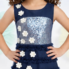 A sleeveless navy blue dress with a sequined silver bodice, ruffled skirt, and white flower appliqués, shown on a child model.