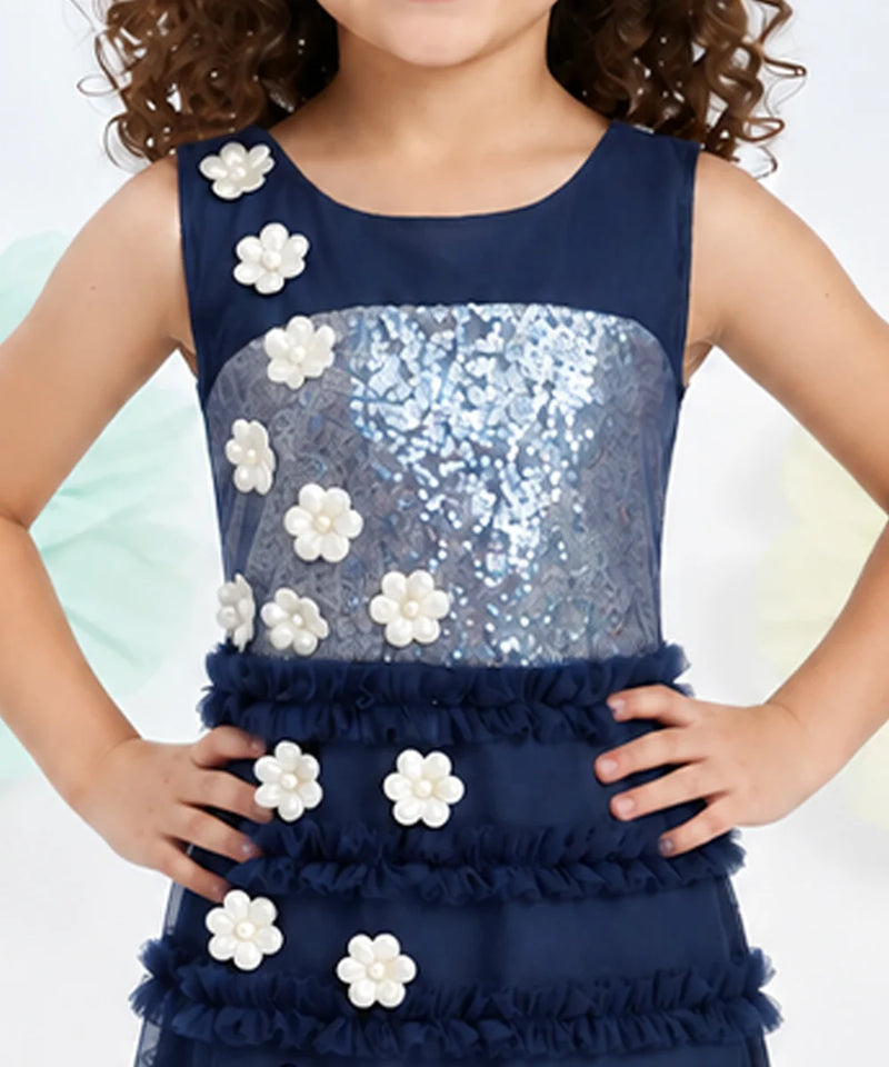 A sleeveless navy blue dress with a sequined silver bodice, ruffled skirt, and white flower appliqués, shown on a child model.