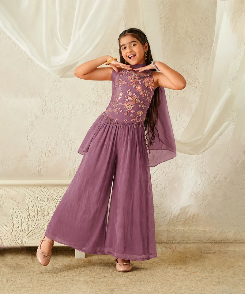 Young girl wearing a purple embroidered dress against a plain background