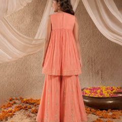 Woman in a peach traditional outfit standing in front of draped fabric with flowers on the ground.