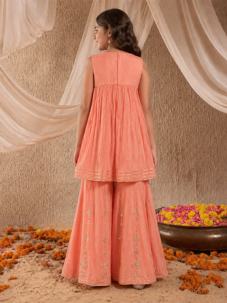Woman in a peach traditional outfit standing in front of draped fabric with flowers on the ground.