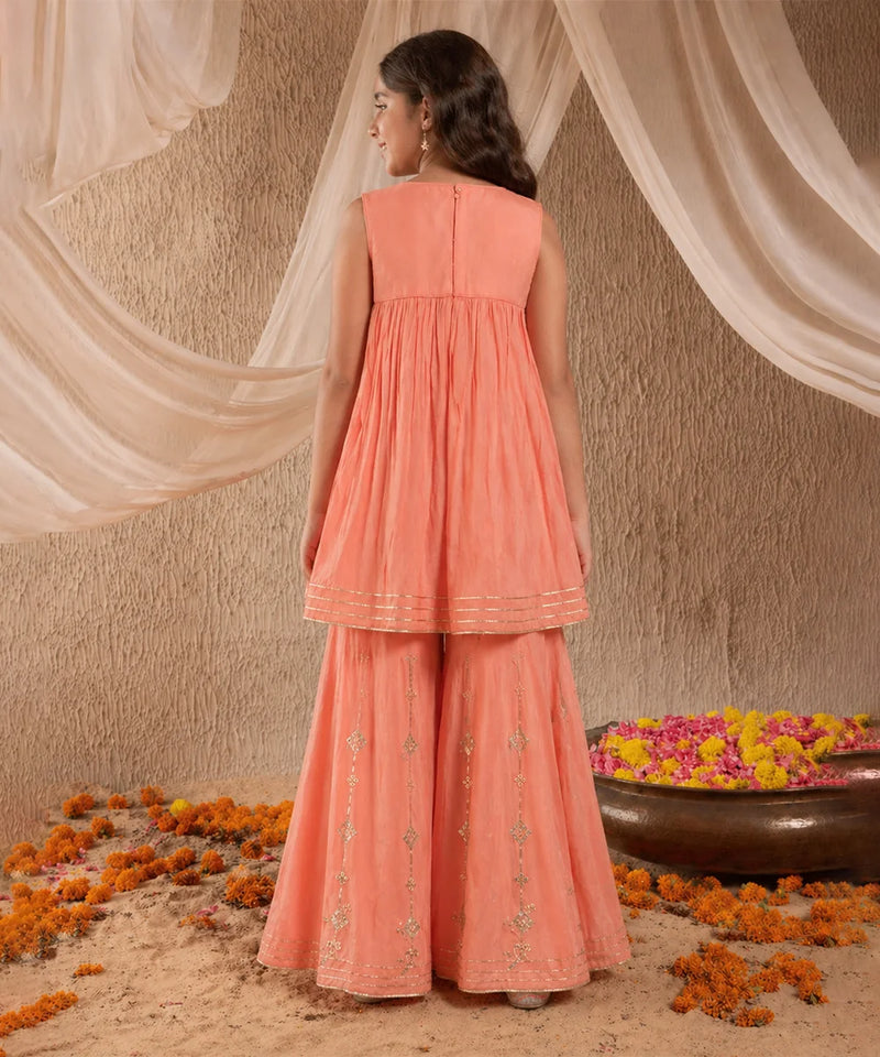 Woman in a peach traditional outfit standing in front of draped fabric with flowers on the ground.