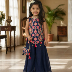 Young girl in a traditional outfit with floral top and navy skirt standing indoors.