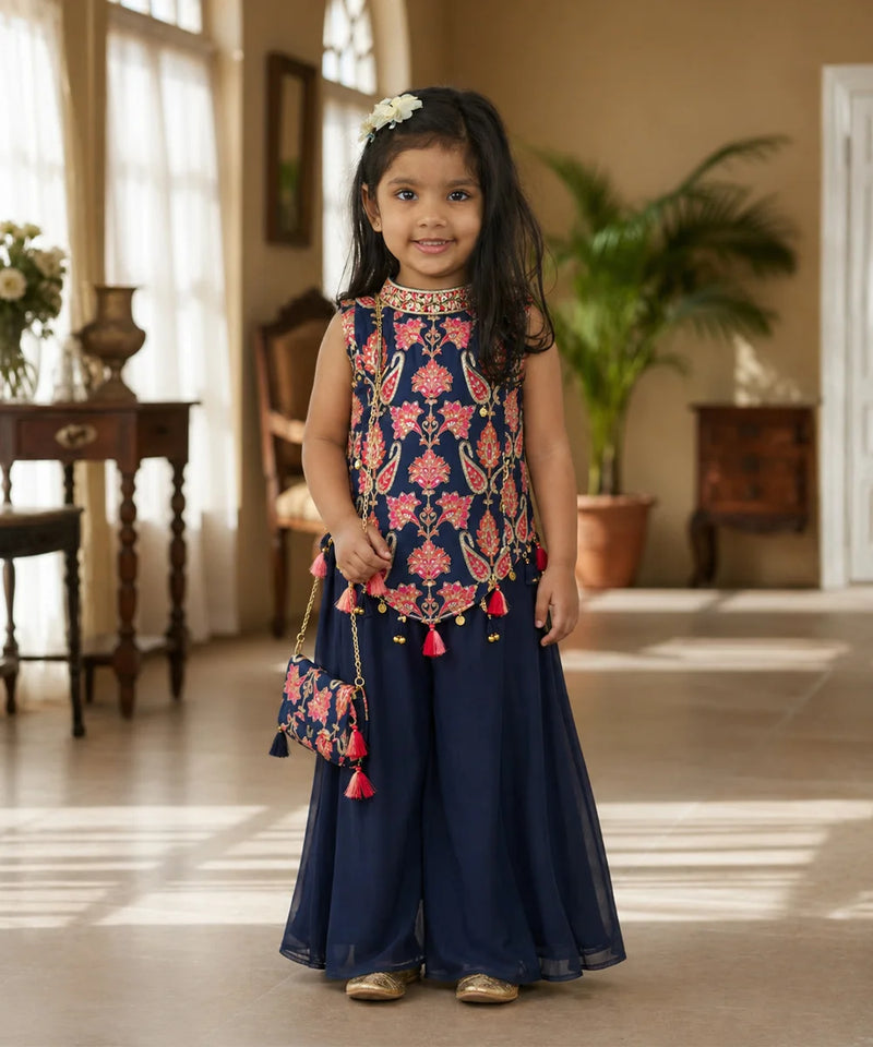 Young girl in a traditional outfit with floral top and navy skirt standing indoors.