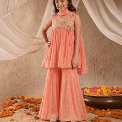 Young girl in a peach traditional outfit with floral decorations and draped fabric in the background.