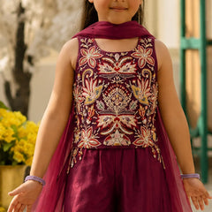 Young girl in a maroon embroidered outfit standing outdoors with blurred background
