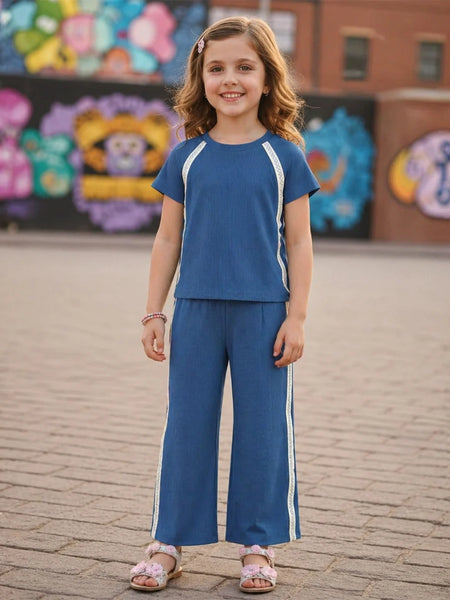Young girl in a blue outfit standing on a brick pavement with colorful murals in the background