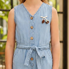 A sleeveless light blue denim-style belted dress with a V-neck and front buttons, shown on a model. The dress features a small decorative cherry embellishment on the chest.
