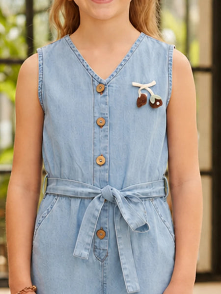 A sleeveless light blue denim-style belted dress with a V-neck and front buttons, shown on a model. The dress features a small decorative cherry embellishment on the chest.