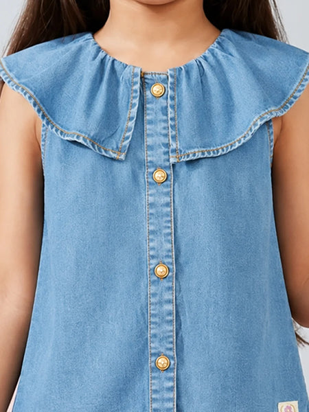 A close-up of a child wearing a light blue denim sleeveless top with a large ruffled collar and gold-tone buttons down the front.