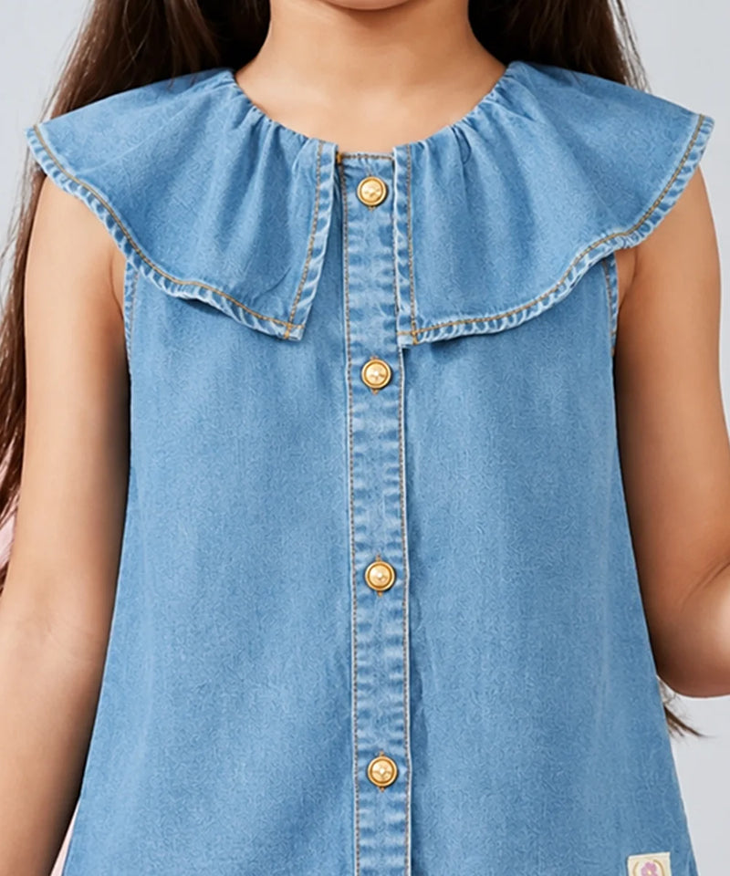 A close-up of a child wearing a light blue denim sleeveless top with a large ruffled collar and gold-tone buttons down the front.