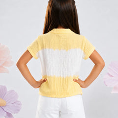 A young girl viewed from behind wearing a yellow and white horizontally striped crinkle-textured short-sleeve top and white shorts, standing against a light gray background with decorative flower graphics.