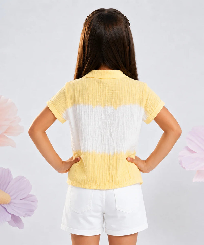 A young girl viewed from behind wearing a yellow and white horizontally striped crinkle-textured short-sleeve top and white shorts, standing against a light gray background with decorative flower graphics.