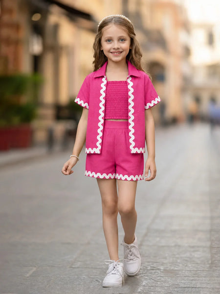 A young girl walking down a blurred city street wearing a bright pink two-piece outfit with white zigzag trim, consisting of a short-sleeve collared top and matching shorts.