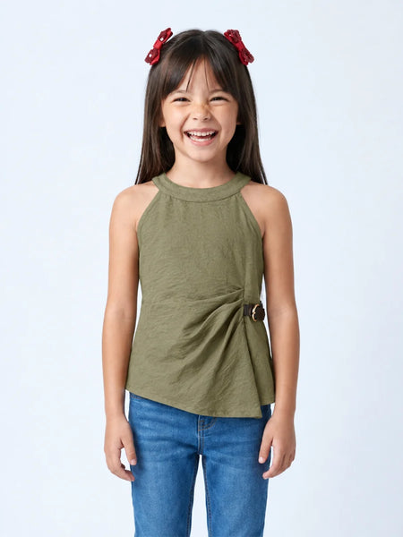 A young girl with dark hair and red bow clips is smiling, wearing an olive green sleeveless wrap-style top with blue jeans against a light gray studio background.