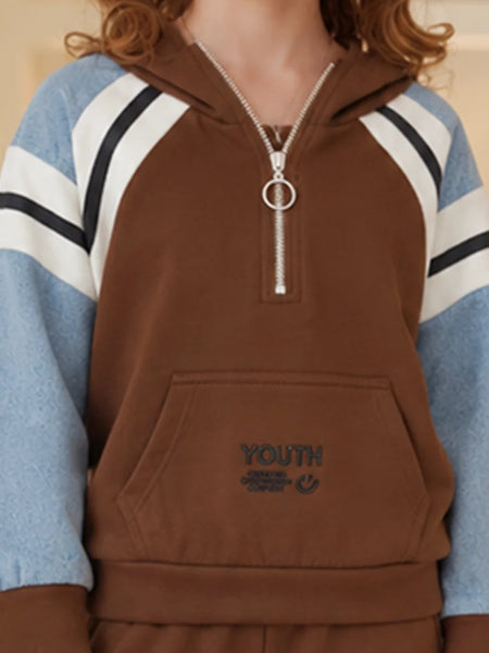 A person wearing a brown half-zip hoodie with light blue sleeves featuring white and black stripes, and a silver zipper pull with a ring detail. The front has a kangaroo pocket with 'YOUTH' embroidered on it.