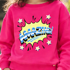 A child wearing a bright pink sweatshirt with a large comic-style 'AMAZING!' graphic in yellow, blue, and white on the front, paired with matching pink bottoms.