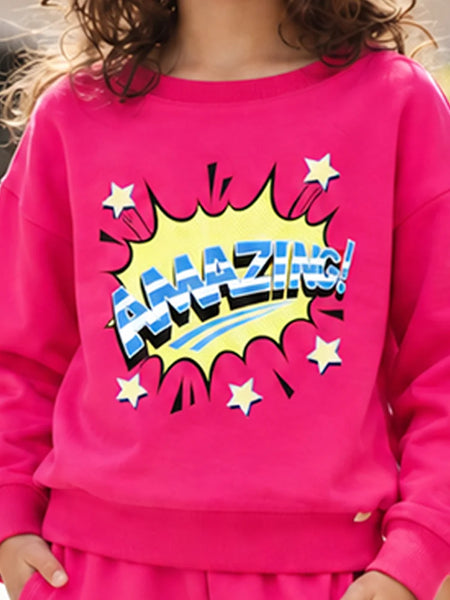 A child wearing a bright pink sweatshirt with a large comic-style 'AMAZING!' graphic in yellow, blue, and white on the front, paired with matching pink bottoms.