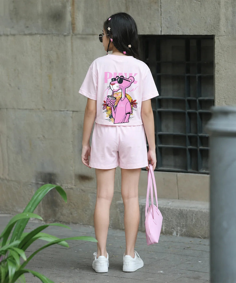 A child wearing a light pink short-sleeve t-shirt and matching shorts, viewed from behind. The back of the outfit features a large graphic print of the Pink Panther holding a drink.