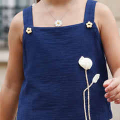 A close-up of a child wearing a navy blue sleeveless top with thick shoulder straps, small yellow flower embellishments, and a large white flower applique on the front.