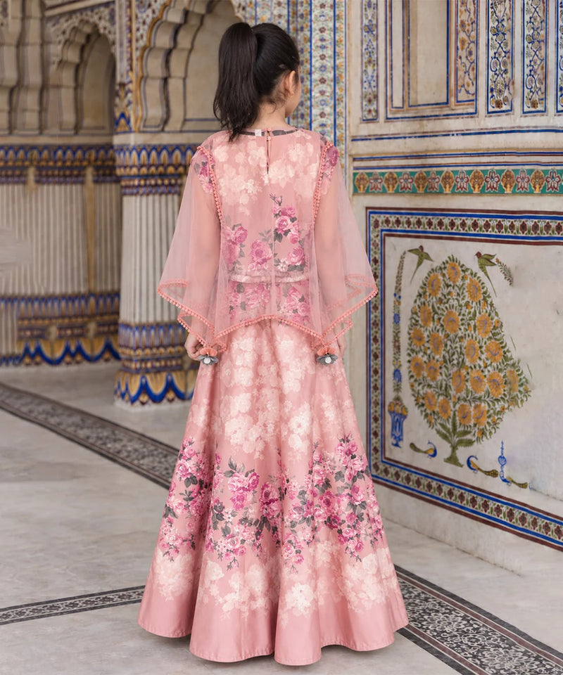 A woman viewed from behind wearing a pink floral traditional gown with sheer draped sleeves, standing in an ornate architectural hallway with decorative tiled walls.