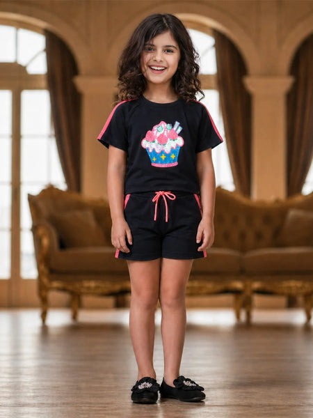 Young girl wearing a black outfit with a colorful design in a room with brown furniture.