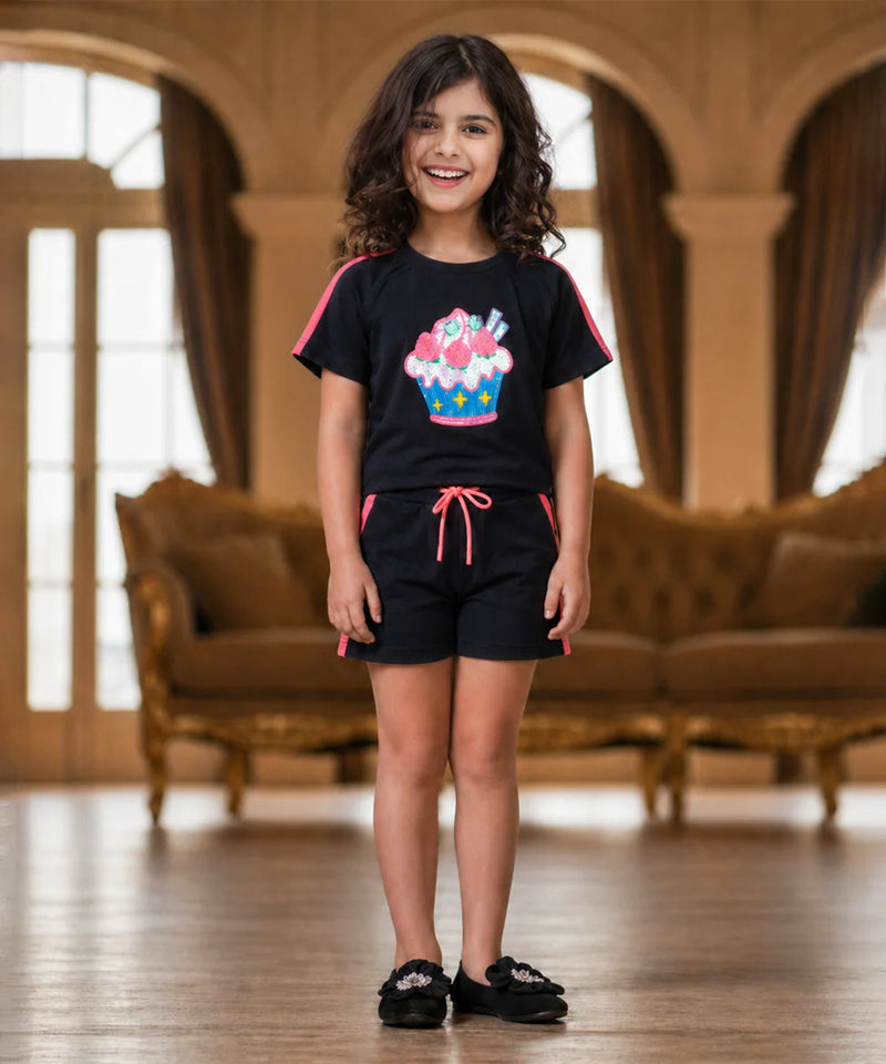 Young girl wearing a black outfit with a colorful design in a room with brown furniture.