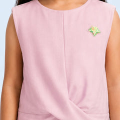 A sleeveless light pink top with a twisted hem detail, worn by a model. The top features a small green and yellow embroidered star on the left chest.