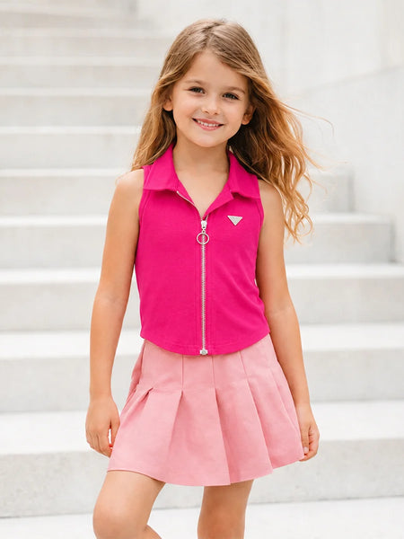 A young girl with long light brown hair stands on light gray concrete steps, wearing a sleeveless bright pink collared zip-front top with a small white geometric logo on the chest and a light pink pleated skirt.