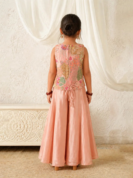 Child wearing a pink traditional outfit with floral patterns against a white curtain background