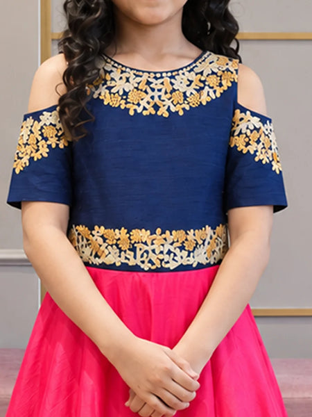 A child wearing a cold-shoulder navy blue top with gold and cream floral embroidery, paired with a bright pink skirt.